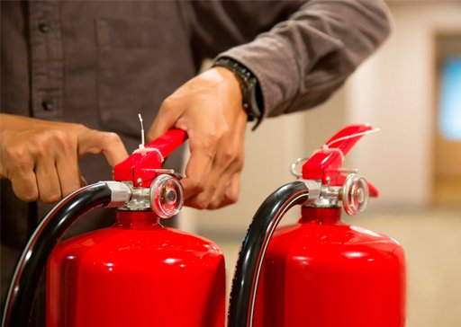 Profissional de brigada da Garra Facilities inspecionando extintores de incêndio, simbolizando prevenção e resposta rápida a emergências.